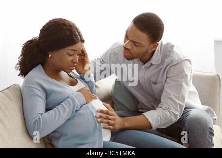 Donna nera incinta che si sente male, marito preoccupato seduto accanto a lei Foto Stock
