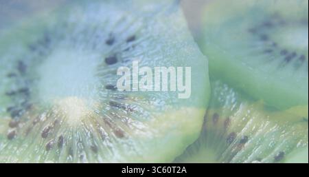 Le fette di kiwi sovrapposte si illuminano di polpa verde brillante sul piatto, con una texture lucida Foto Stock