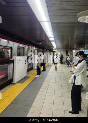 Pendolari in attesa sulla piattaforma della metropolitana di Osaka con treno in arrivo, Giappone Foto Stock