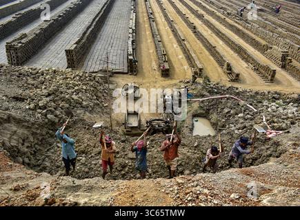Gokul, Bangladesh - 27 novembre 2017: Veduta dei lavoratori che lavoravano in una fossa di argilla, le loro figure incorniciate contro le torreggianti pile di mattoni essiccati sotto il cielo aperto. Foto Stock