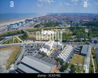 Veduta aerea degli edifici moderni di colore bianco che contrastano con i lussureggianti parchi verdi e la lontana spiaggia di sabbia che si fonde nel Mare del Nord, Dunkerque, Francia. Foto Stock