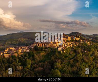 Vista aerea dell'antica città collinare di Montepulciano con i suoi edifici baciati dal sole in pietra, annidata tra le dolci colline verdi sotto un cielo colmo di luce dorata, Montepulciano, Toscana, Italia. Foto Stock