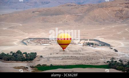 La mongolfiera scende nei pressi di un villaggio nel deserto e di un'oasi verde a Luxor, in Egitto. Foto Stock