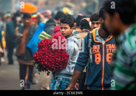 Kolkata, India - 28 gennaio 2023: Veduta di un giovane uomo tra una folla affollata, che regge un vivace bouquet di rose rosse, uno spruzzo di colore contro la m Foto Stock