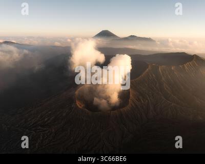 Vista aerea del maestoso vulcano del Monte Bromo che fuma con le profondità scure del cratere che contrastano con le eteree zampe di nuvole, il Parco Nazionale di Bromo Tengger Semeru, Giava Orientale, Indonesia. Foto Stock