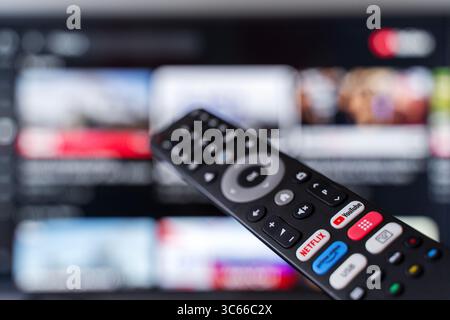 Tbilisi, Georgia - 2 luglio 2025: Foto ravvicinata di un telecomando smart TV con pulsanti dedicati per piattaforme di streaming popolari come Netflix, YouTube e Amazon prime, con uno schermo televisivo sfocato sullo sfondo. Rappresenta il consumo dei moderni media digitali, i servizi basati su abbonamento e l'intrattenimento on demand. Ideale per contenuti tecnologici, in streaming, binge-watching o media lifestyle. Foto Stock