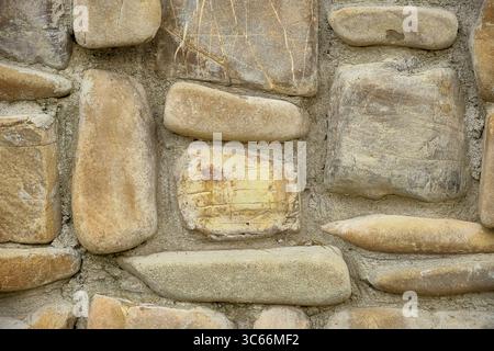 Pareti in pietra naturale con forme irregolari e tonalità terrose, perfette per sfondi e dettagli architettonici Foto Stock