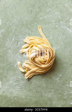 Tagliatelle fresche crude fatte in casa su una superficie di lavoro infarinata. Foto Stock