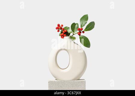 agnello natalizio con bacche rosse in vaso bianco. Decorazione naturale invernale su sfondo bianco, spazio per copie. Foto Stock