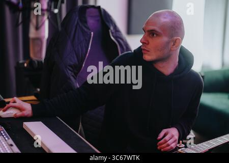 Uomo concentrato che lavora in studio di musica per regolare l'audio al computer Foto Stock