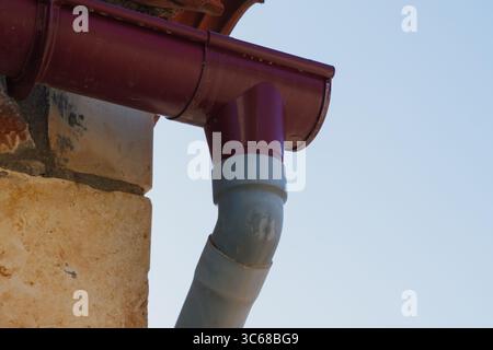 Sistema di drenaggio dell'acqua piovana di un edificio vicino a un muro di pietra, progettato per raccogliere e deviare le precipitazioni dal tetto Foto Stock