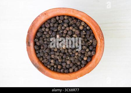 Vista dall'alto verso il basso di una tazza di argilla riempita di grani di pepe nero. Foto Stock