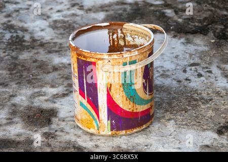 Vecchio secchio di vernice conservato sul pavimento in cemento sul tetto dell'edificio. Foto Stock