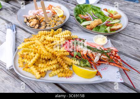 Pranzo presso il ristorante di pesce Osbournes a Leigh-on-Sea, Essex, Regno Unito. Un tavolo estivo con aragosta, patatine fritte tagliate a rughe e piatto di pesce Foto Stock