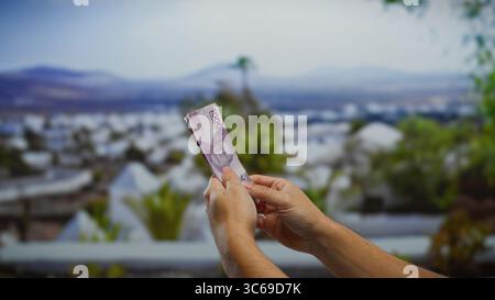 Uomo che tiene banconote in rupia indonesiana all'aperto in una strada cittadina creando un'atmosfera urbana di transazioni commerciali con cambio valuta. Foto Stock