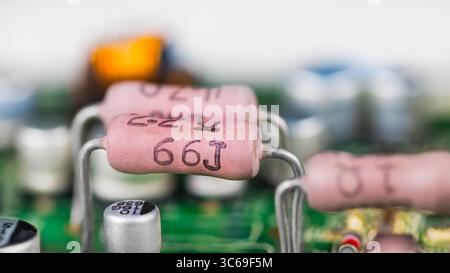 Vista laterale dei resistori rosa e dei condensatori bianchi su un circuito stampato verde. Primo piano di vari componenti elettronici su sfondo sfocato della scheda a circuito stampato. Foto Stock