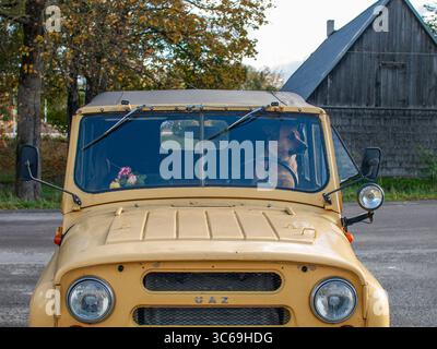 Un grande cane siede al posto di guida di una jeep sovietica UAZ dietro il volante, guardando verso l'esterno. Fotografato dall'esterno attraverso la finestra. Foto Stock