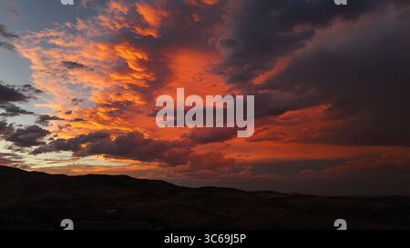Veduta aerea di un suggestivo cielo al tramonto che si illumina di ardenti sfumature arancioni in contrasto con le scure e ondulate colline sottostanti, Reno, Nevada, Stati Uniti. Foto Stock