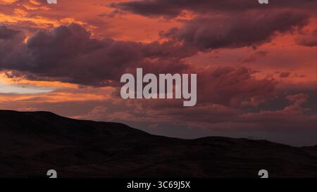 La vista aerea di un tramonto sereno dipinge il cielo con sfumature di fuoco sopra le colline scure e ondulate che gettano ombre lunghe, Reno, Nevada, Stati Uniti. Foto Stock