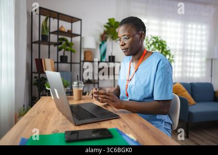 Dottoressa afroamericana concentrata che lavora su un portatile a casa Foto Stock