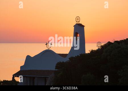 Porto Cervo, Costa Smeralda, Gallura, Sardegna, Italia. Ammira dalla collina l'iconica chiesa di Stella Maris, l'alba, il sole che splende attraverso il campanile. Foto Stock