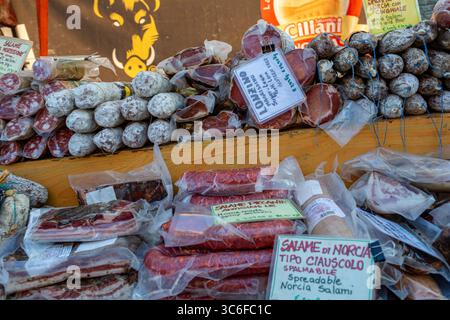 Una vivace esposizione di salumi assortiti su una stalla di legno, con vari salumi e salsicce con etichette, che mettono in risalto la cultura gastronomica tradizionale Foto Stock