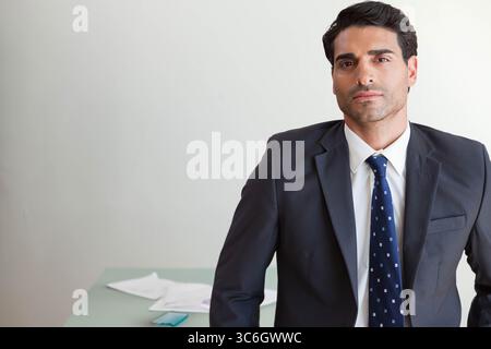 Uomo medio adulto in tuta in piedi alla scrivania dell'ufficio che esamina i documenti e controlla lo smartphone, copia dello spazio. Professionale, aziendale, moderno, minimalista, busin Foto Stock