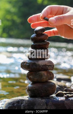 Primo piano di Hands Stacking Rocks by a Stream in un tranquillo ambiente naturale Foto Stock