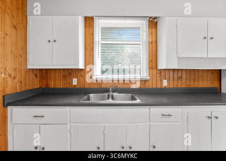 Cucina con armadi bianchi e lavello. Il lavello è in acciaio inox e il bancone è nero Foto Stock