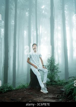 Autoritratto di un uomo seduto su un ceppo d'albero in una foresta nebbiosa a Darjeeling, in India. Catturati durante la stagione dei monsoni con un filtraggio della luce soffusa. Foto Stock