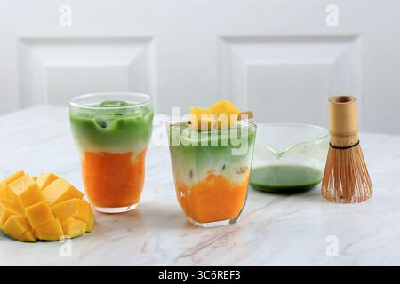 Due bicchieri di latte Matcha di mango Iced fatto in casa sul tavolo bianco Foto Stock