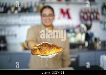 Una persona offre un croissant al bancone di un caffè con sfondo sfocato, Cremona, Italia 25 luglio 2025 Foto Stock