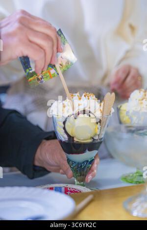 Una deliziosa sundae di gelato con panna e waffle è tenuta a mano, salsa di cioccolato visibile, retro Freizeitpark Poppeltal Riesenrutschbahn, Enzkloes Foto Stock
