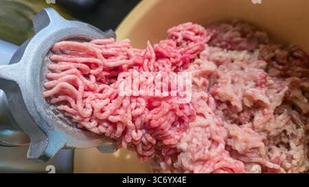 Macinacaffè con carne macinata fresca sul tavolo della cucina. Primo piano della carne macinata che cade in un recipiente di metallo. Messa a fuoco selettiva. Foto Stock