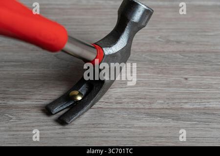 Immagine ravvicinata di un martello a baionetta con impugnatura rossa che aggancia un chiodo in ottone su una superficie in legno Foto Stock