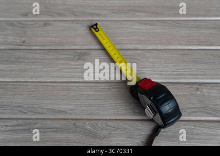 Primo piano di un nastro di misurazione giallo esteso su una superficie in legno, con segni di centimetri chiari Foto Stock