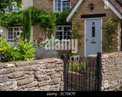Affascinante cottage in pietra nel villaggio di Hanslope, Buckinghamshire, Regno Unito; con un cottage giardino frontale, muro di pietra e cancello di ferro in un ambiente rurale Foto Stock