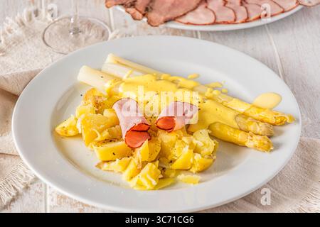 Piatto con asparagi, patate, prosciutto e salsa hollandaise su sfondo bianco di legno Foto Stock