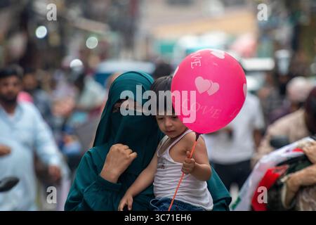 Srinagar, India. 1 agosto 2025. Donna Kashmiri vestita di hijab tiene suo figlio mentre cammina in un mercato durante le calde giornate estive nella capitale estiva. Credito: SOPA Images Limited/Alamy Live News Foto Stock
