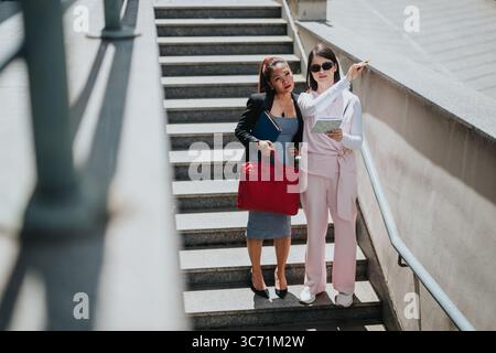 Due donne che collaborano su una scala, discutono di progetti e condividono appunti Foto Stock