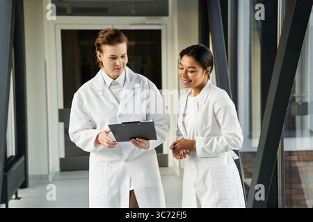 Due medici femminili si sono impegnati in una discussione mentre camminavano attraverso un ospedale contemporaneo. Foto Stock