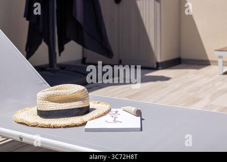 Cappello di paglia e libro posti su un lettino, evocando un'atmosfera di vacanza tranquilla. Foto Stock