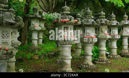 Lanterne di pietra con bambole Daruma al tempio Katsuo-ji, Minoh, Giappone - simbolo di perseveranza e preghiera Foto Stock