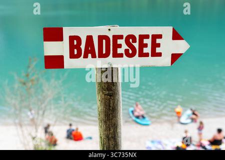 Germania - 30 luglio 2025: FOTOMONTAGGIO, Un cartello che punta in direzione del lago balneabile - un luogo popolare per attività ricreative, sportive e estive in acqua per grandi e piccini. *** FOTOMONTAGE, Ein Hinweisschild zeigt Richtung Badesee ein beliebter Ort für Erholung, Sport und sommerliche Aktivitäten am Wasser für Groß und Klein. Foto Stock