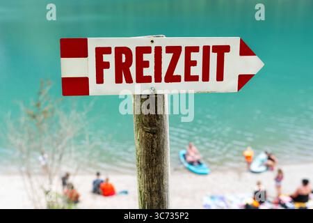 Germania - 30 luglio 2025: FOTOMONTAGGIO, Un cartello con la scritta Freizeit punta alla spiaggia - simbolo del relax estivo in riva all'acqua, rallentando e trascorrendo il tempo con la famiglia o gli amici. *** FOTOMONTAGE, Ein Schild mit der Aufschrift Freizeit zeigt auf den Badestrand ein Sinnbild für sommerliche Erholung am Wasser, Entschleunigung und gemeinsame Zeit mit Familie oder Freunden. Foto Stock