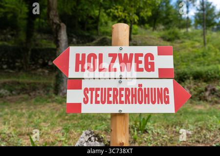 Germania - 30 luglio 2025: FOTOMONTAGGIO, Un cartello satirico mostra un aumento delle tasse e un percorso in legno - un'immagine simbolica politica per criticare le decisioni fiscali e aumentare gli oneri fiscali. *** FOTOMONTAGE, Ein satirisches Wegweiserschild zeigt Steuererhöhung und Holzweg ein politisches Symbolbild zur Kritik an fiskalischen Entscheidungen und steigender Abgabenbelastung. Foto Stock