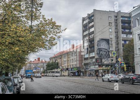 Il cielo estivo sovrasta una via di Kaliningrad con blocchi di pannelli sovietici, un murale di astronauti sovietici, binari del tram e pedoni su ciottoli. Foto Stock