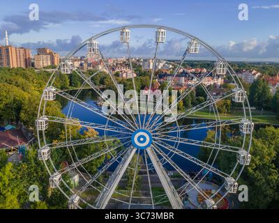Panoramica ruota panoramica del parco divertimenti Upper Pond di Kaliningrad, che si riflette in acqua contro un cielo parzialmente nuvoloso. Foto Stock