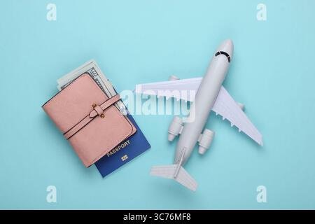 Composizione piatta della corsa su sfondo blu. Figurina dell'aereo, passaporto, portafoglio con dollari. Attività ricreative, vacanze e turismo, concetto di minimalismo. Foto Stock