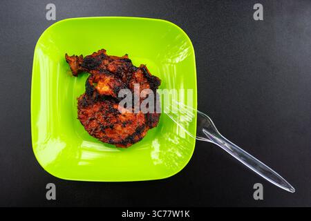 Piastra di plastica verde con un pezzo di carne grigliata succosa su sfondo nero. Carne fritta in stoviglie monouso. Foto di alta qualità Foto Stock